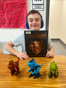 Student posing with figures from the book he is holding. He has headphones covering his ears.