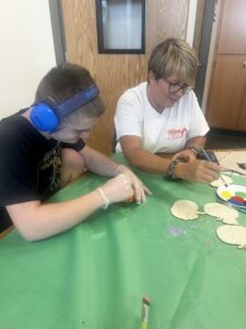 A Unified Art student working on a project with a teacher, the student is wearing sound mufflers