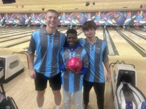 Three Unified Bowling students smiling together at a bowling alley; one is holding a red bowling ball